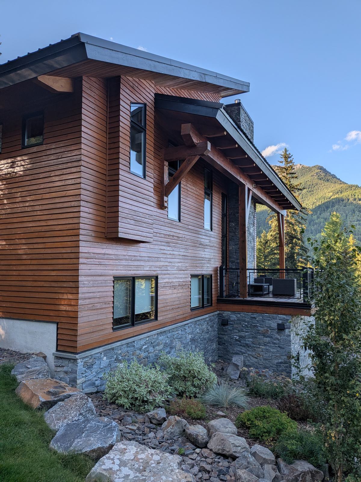 Modern Fernie home with freshly stained cedar siding, timber beams and a slate stone base, mountains behind